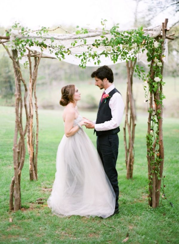 a bride and groom are standing under an arch made out of branches with greenery