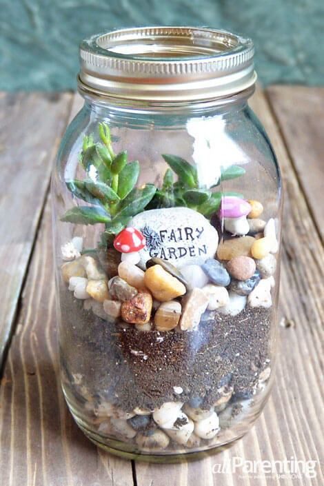 a jar filled with rocks and plants sitting on top of a wooden table