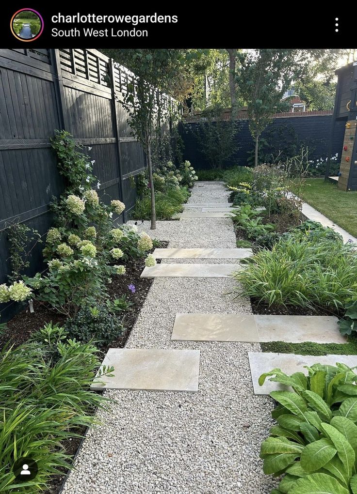 a garden with lots of green plants and gravel path leading to the side of a house