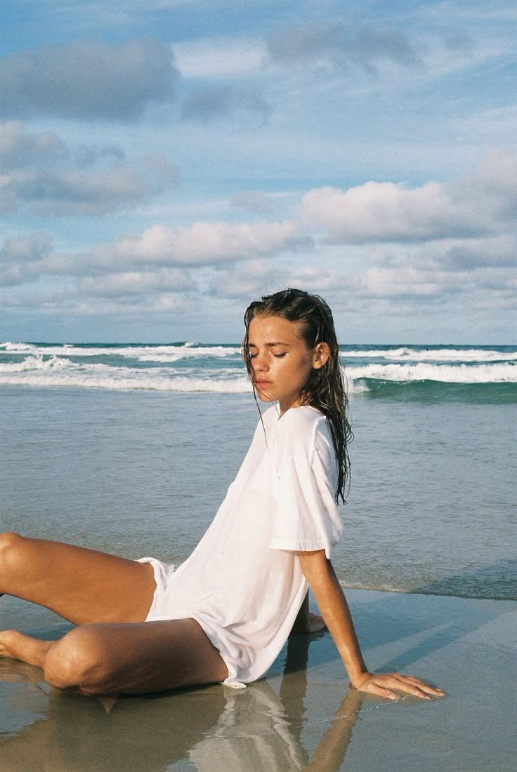 a woman is sitting on the beach with her legs spread out and feet in the water