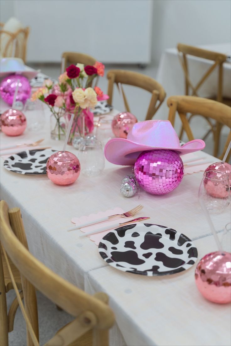 the table is set with pink and black plates, cow print napkins, cowboy hats, and flowers