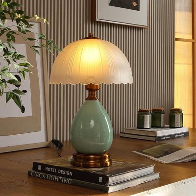 a green lamp sitting on top of a wooden table next to books and a potted plant