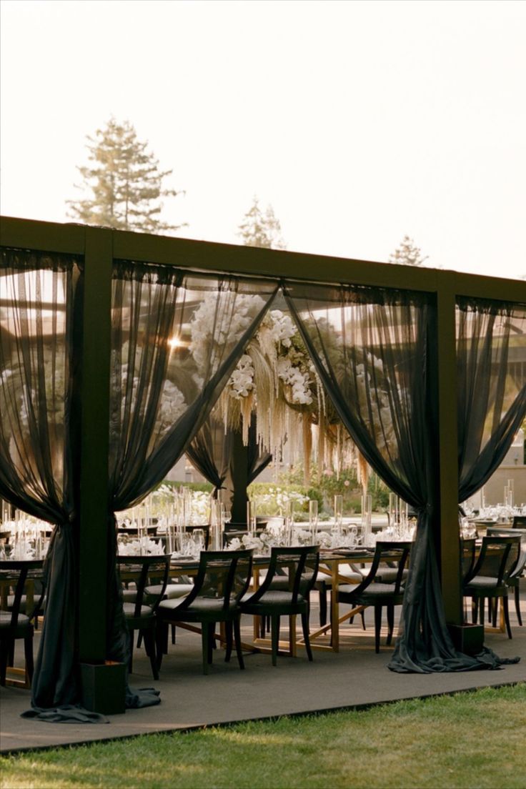 an outdoor dining area with tables and chairs covered in black drapes, surrounded by tall trees