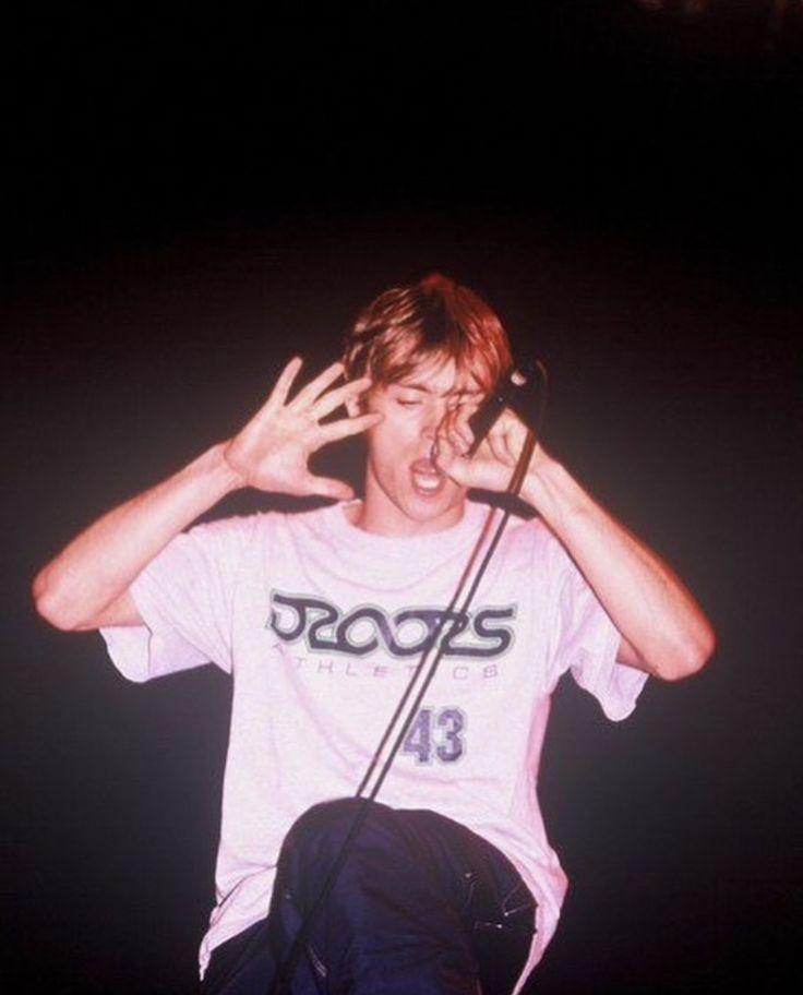 a young man with his hands up in the air while singing into a microphone at a concert