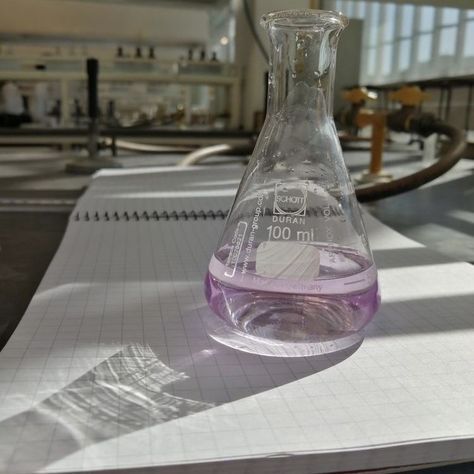 a flask filled with purple liquid sitting on top of a white sheet of paper