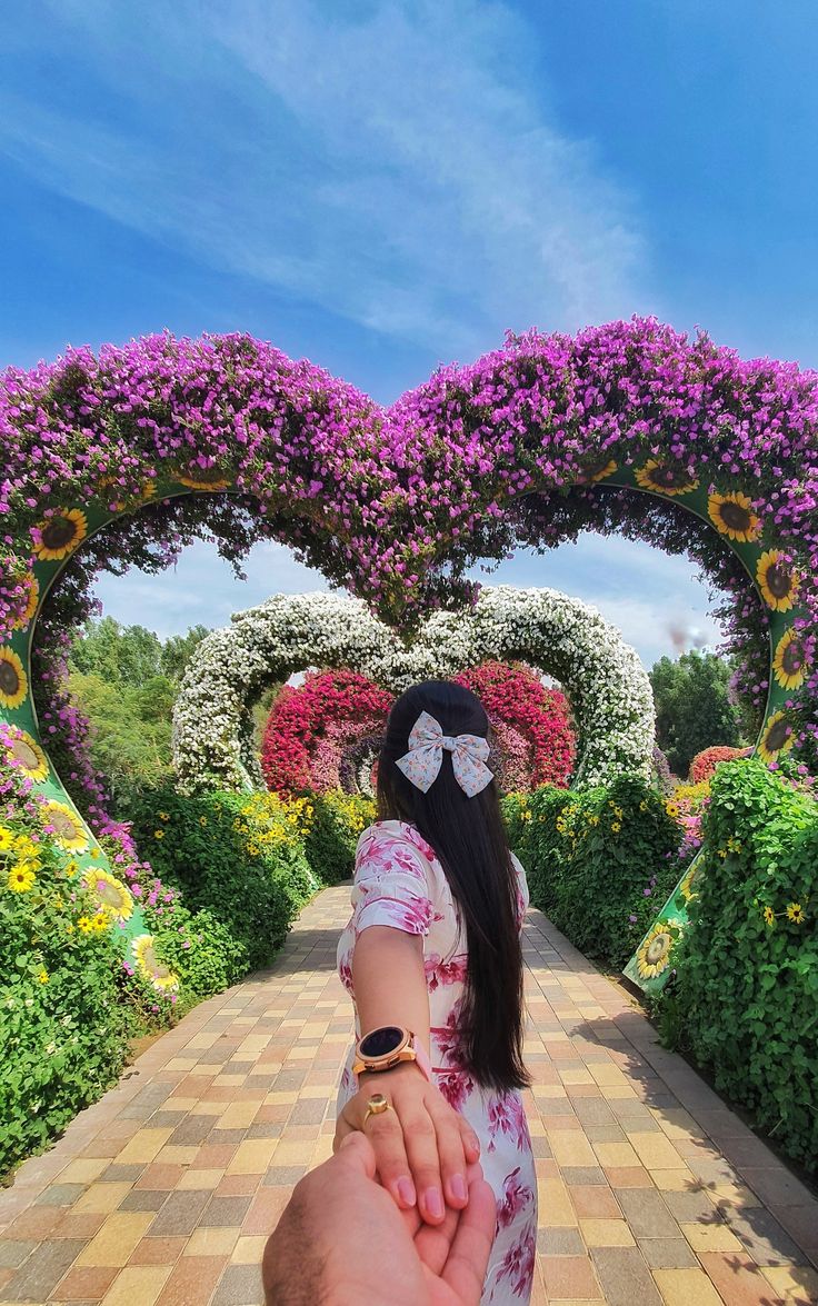 a person holding the hand of another person in front of flowers and hearts shaped archways