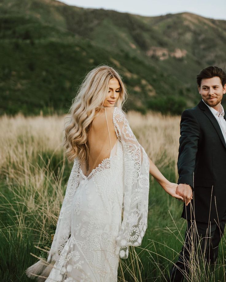 a bride and groom holding hands walking through tall grass