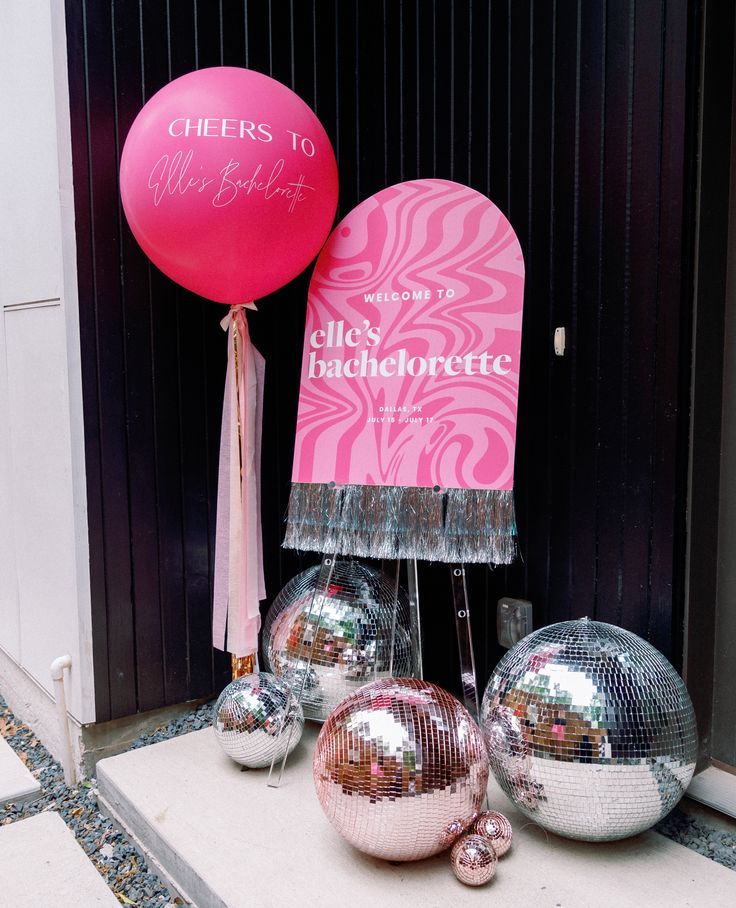 three shiny disco balls and a pink sign are on display outside the entrance to an event