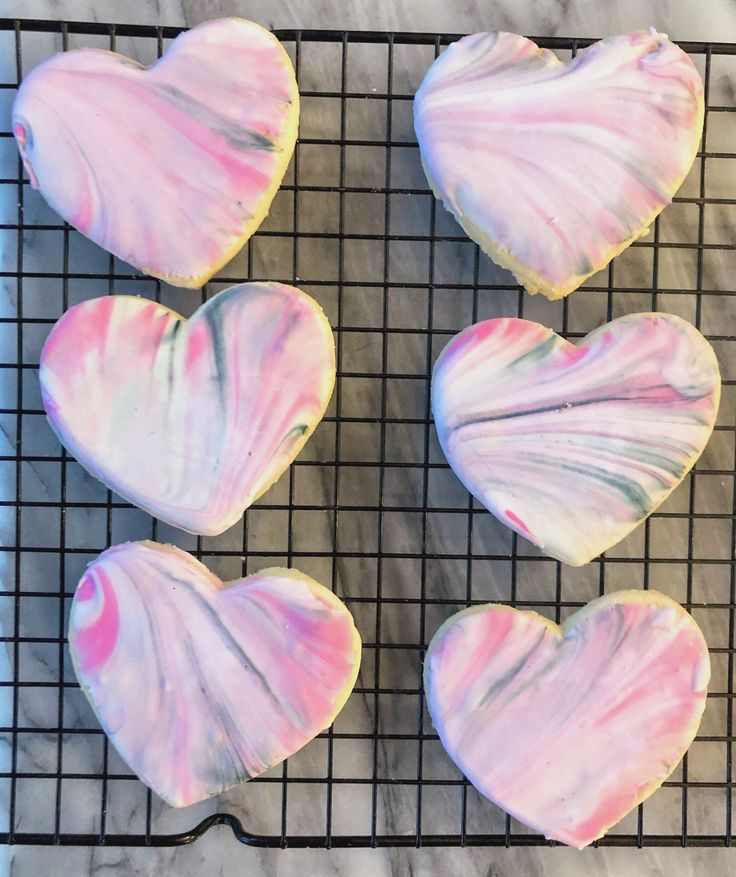 four heart shaped cookies sitting on top of a cooling rack with pink and white icing