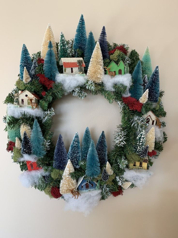 a christmas wreath with houses, trees and snow on the bottom is hanging on a wall