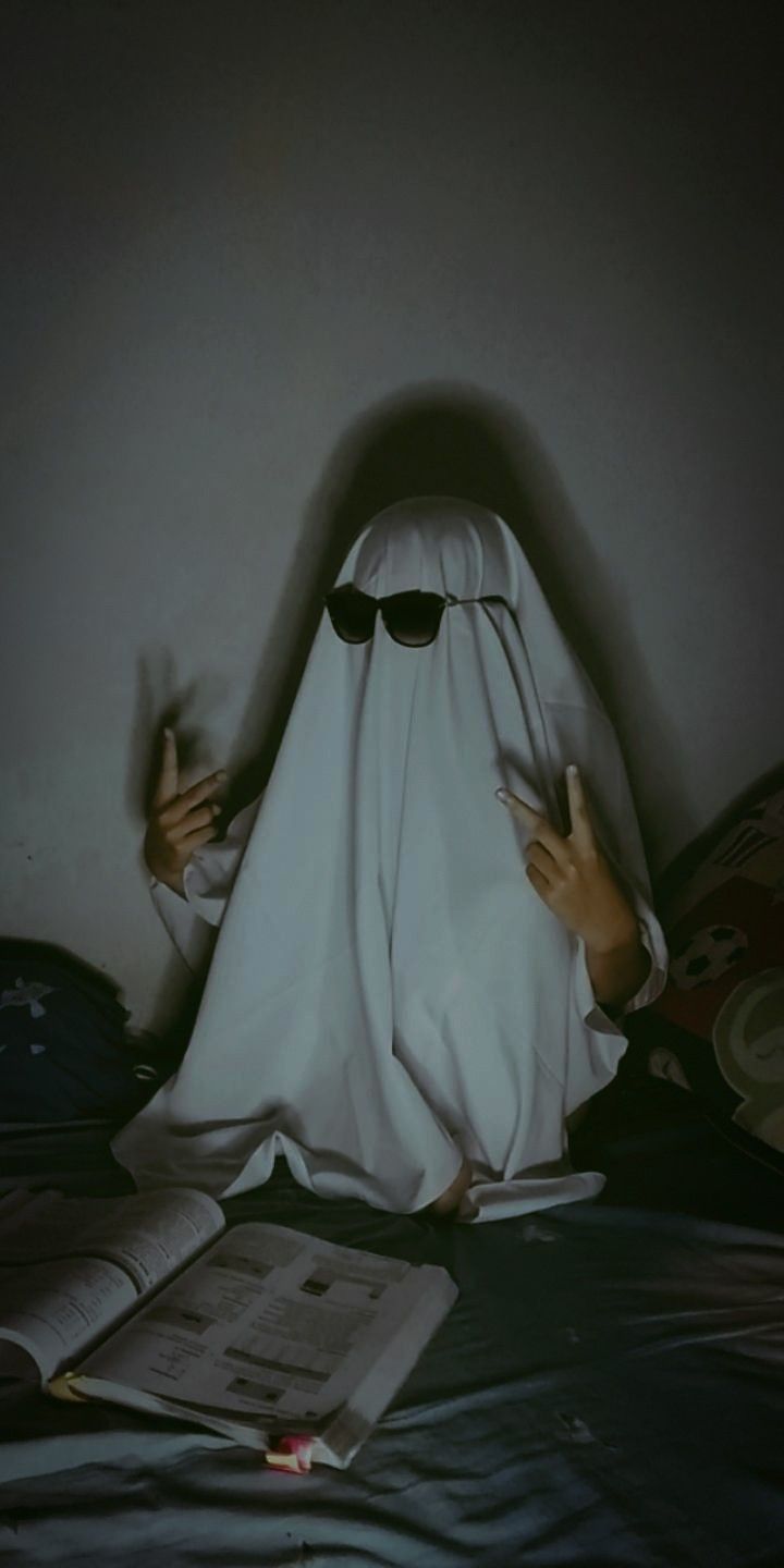 a person in a bed with a white sheet covering their head and hands, reading a book