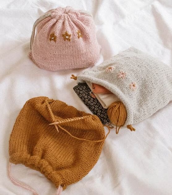 three knitted items are laying on a white bed with a drawstring bag