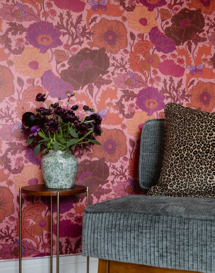 a floral wallpapered room with a leopard print chair and vase filled with flowers