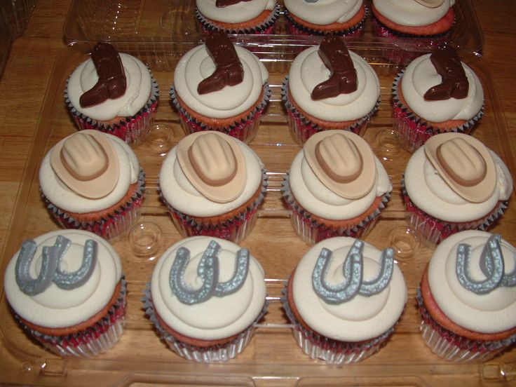 twelve cupcakes with cowboy hats and horseshoes on them are arranged in a display case