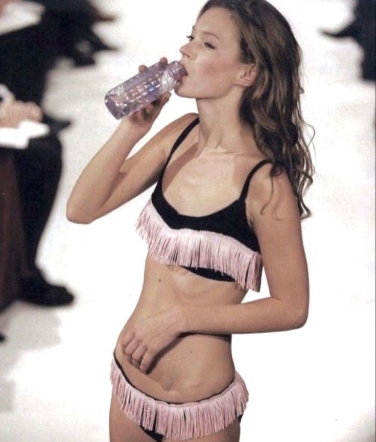 a woman in a bathing suit drinking from a water bottle while standing on the runway