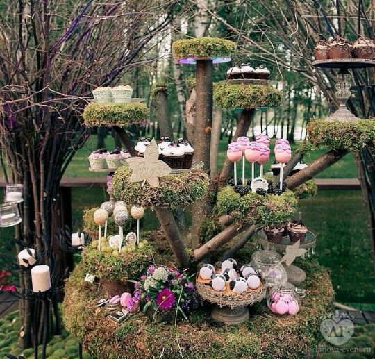 a table topped with lots of cupcakes covered in moss and trees filled with candles