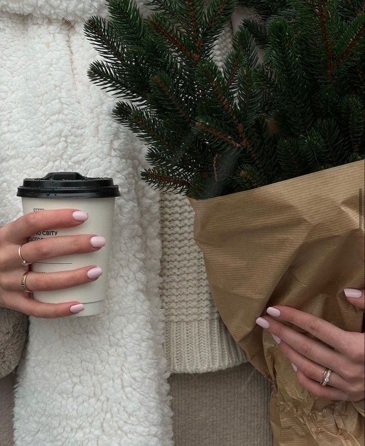 a woman holding a cup of coffee in her right hand and wrapped in a blanket