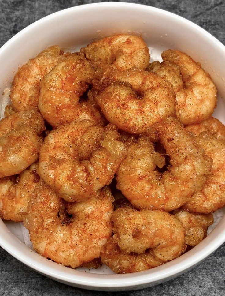 a white bowl filled with fried shrimp on top of a table next to a fork