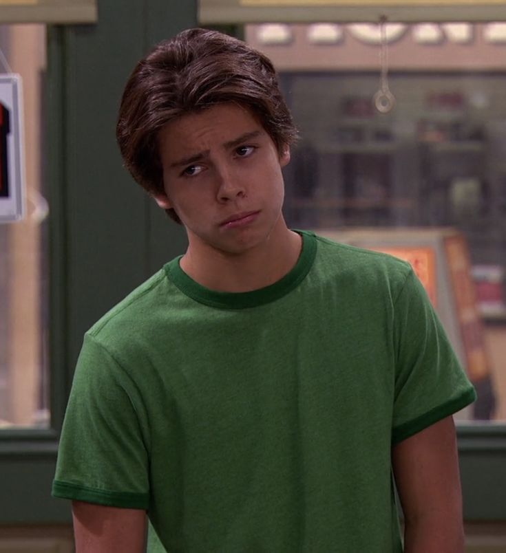 a young man in a green t - shirt is looking at the camera with an angry look on his face