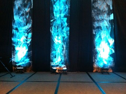 three tall blue lights are lit up on the floor in front of a black curtain