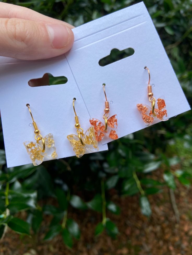 three pairs of earrings are being held up in front of some bushes and greenery