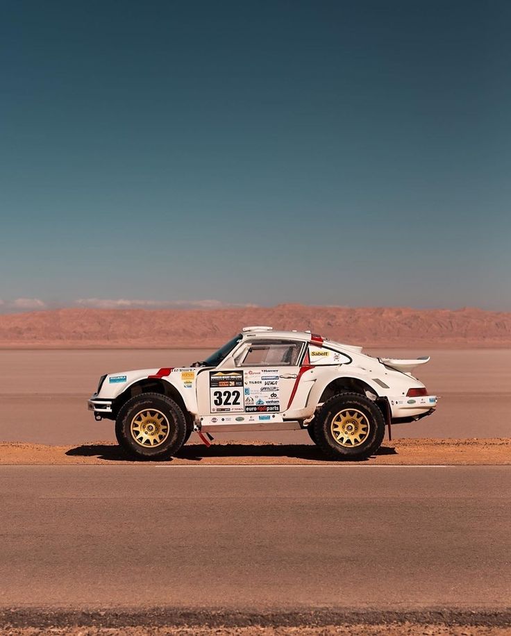 a white rally car driving down the road in front of some desert mountains and blue sky