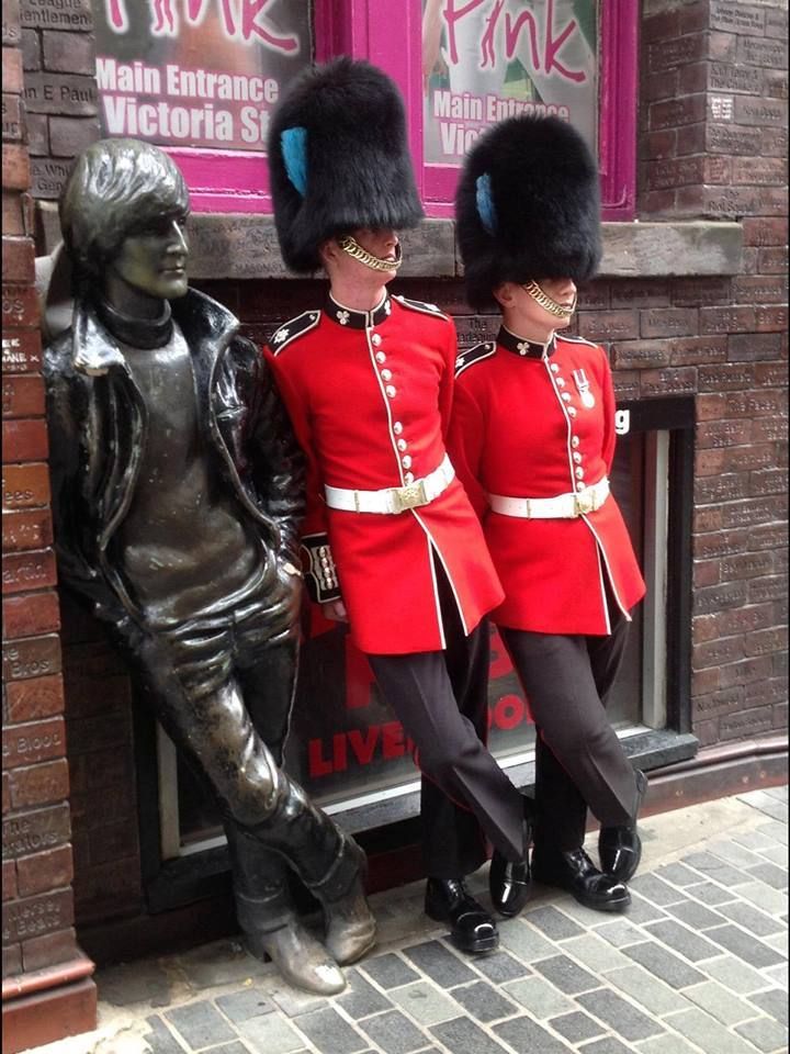 two men dressed in red uniforms standing next to a statue with their hands on each other's hips