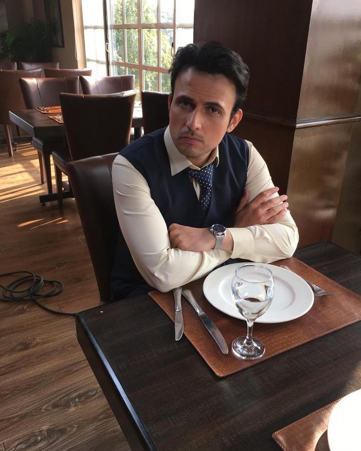 a man sitting at a table with his arms crossed in front of him, wearing a vest and tie