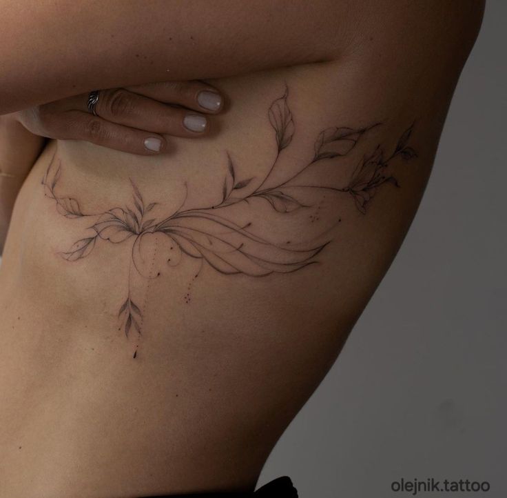 a woman's stomach with tattoos on it and leaves drawn on the side by her