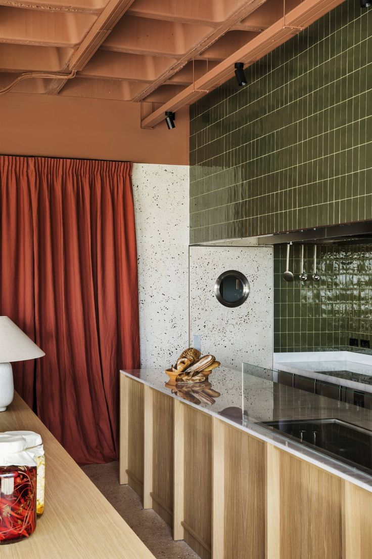 a kitchen with green tile walls and wooden counter tops next to a red curtained window