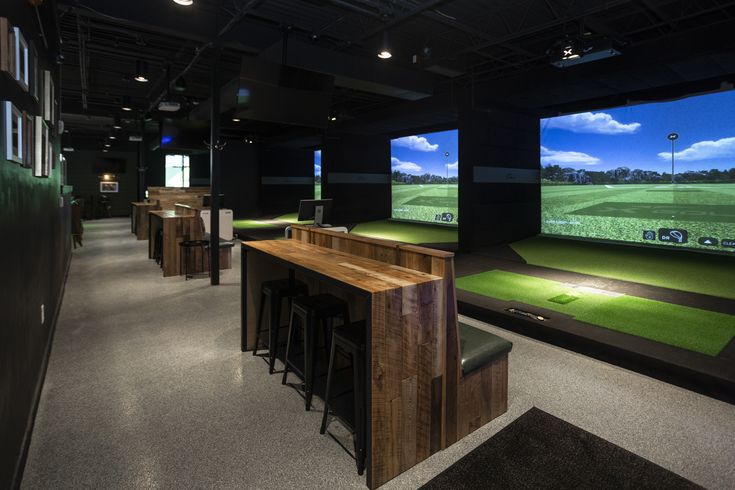 an indoor golf simulator is shown in the dark with green grass on the screen and stools