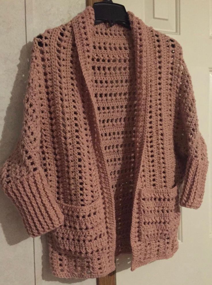 a pink crocheted cardigan hanging on a white door with a wooden hanger