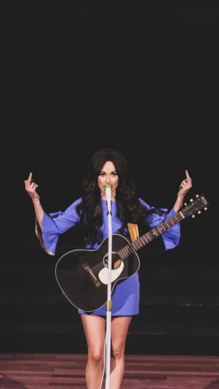 a woman standing on stage holding a guitar