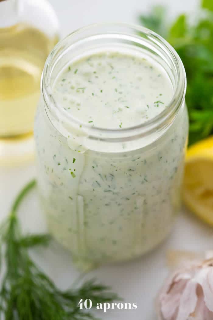 a jar filled with dressing next to lemons and herbs