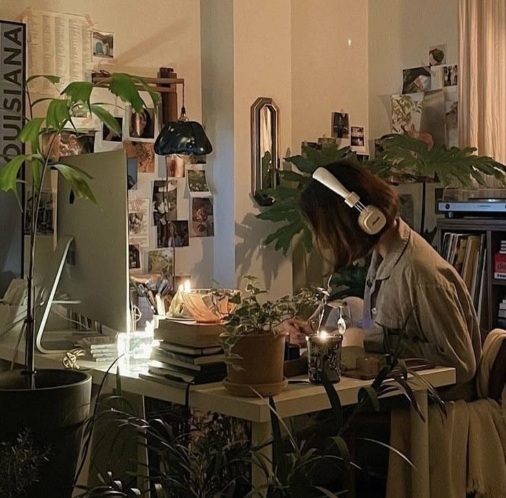 a woman sitting at a desk with headphones on and plants in front of her