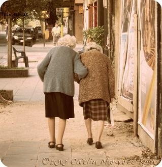 two older women walking down the sidewalk in front of an old building with posters on it