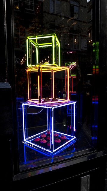 three neon cubes sitting in front of a store window on a city street at night