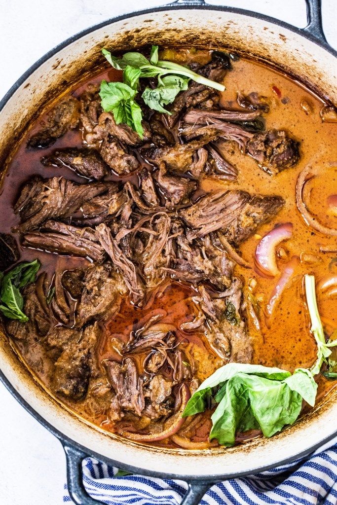 a pot filled with meat and vegetables on top of a stove burner next to a towel