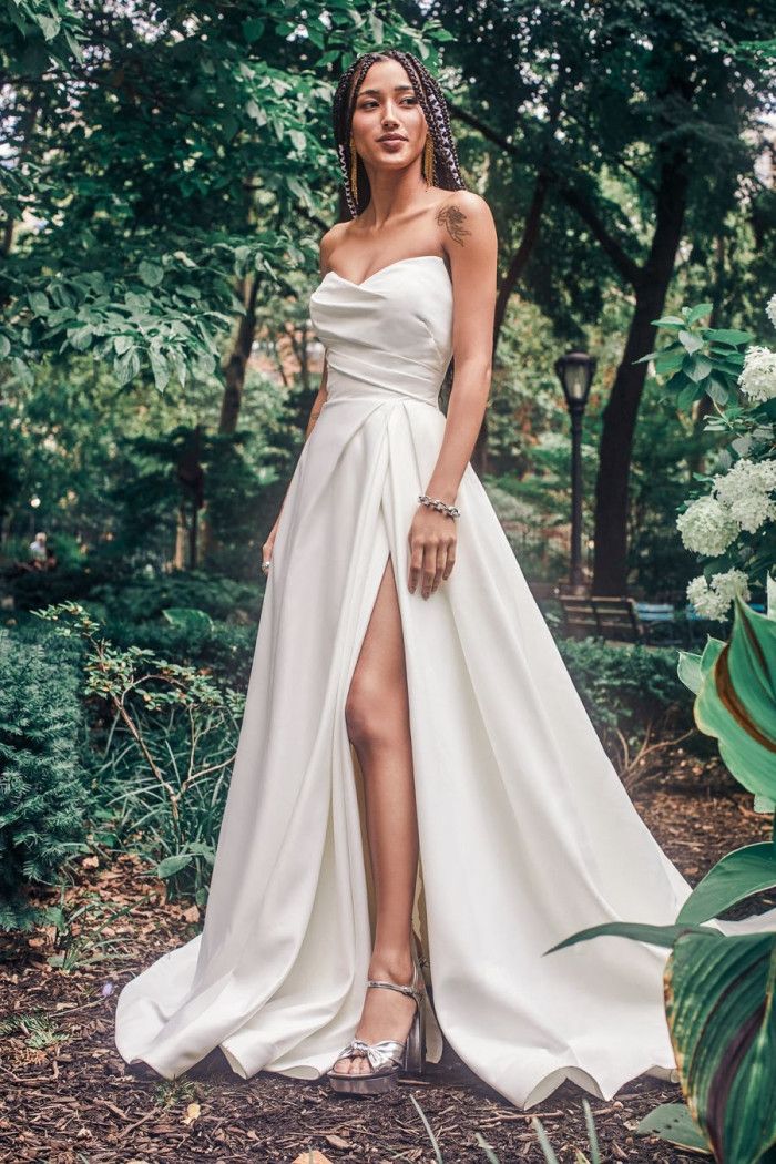 a woman standing in the woods wearing a white dress with high slits on her legs