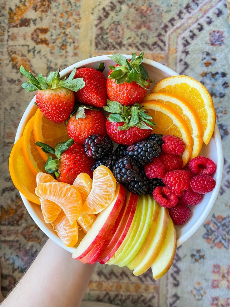 a person holding a white bowl filled with fruit