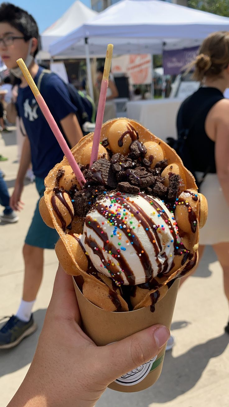 a person holding an ice cream sundae with chocolate and sprinkles on it