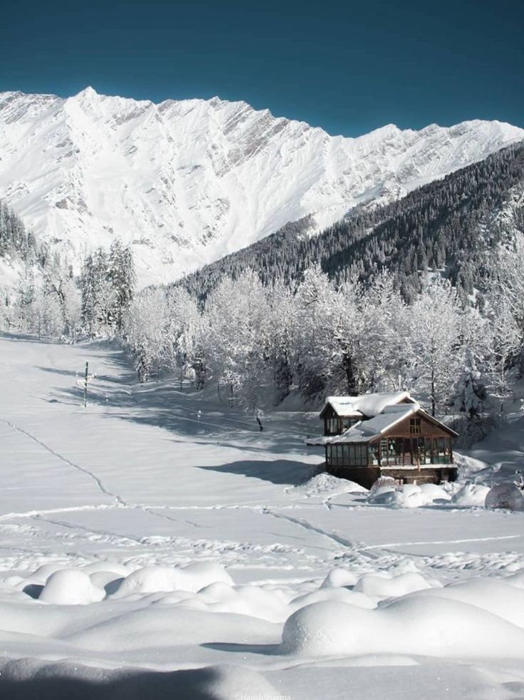 a snowy mountain with a cabin in the foreground and snow covered mountains in the background