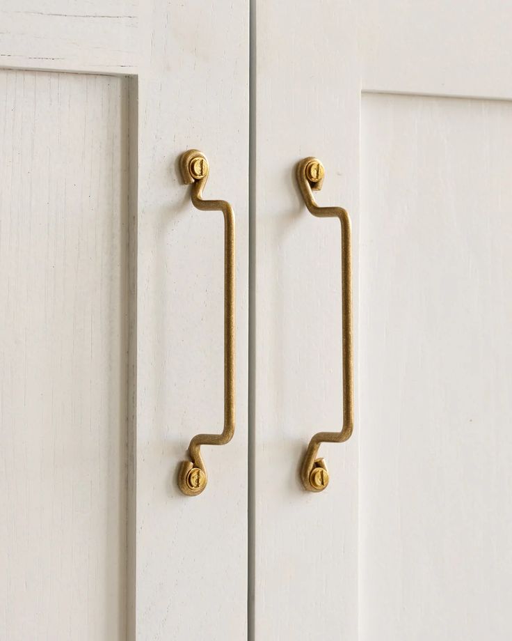 an image of a door handle that is on the side of a white cabinet with gold handles