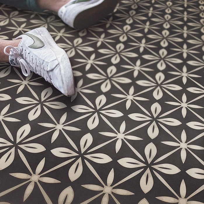 a person's feet standing on a patterned floor with white shoes in front of them