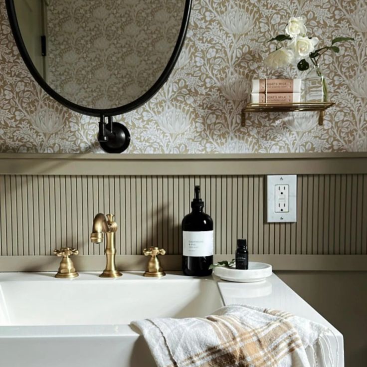 a white sink sitting under a bathroom mirror next to a bottle of wine and soap