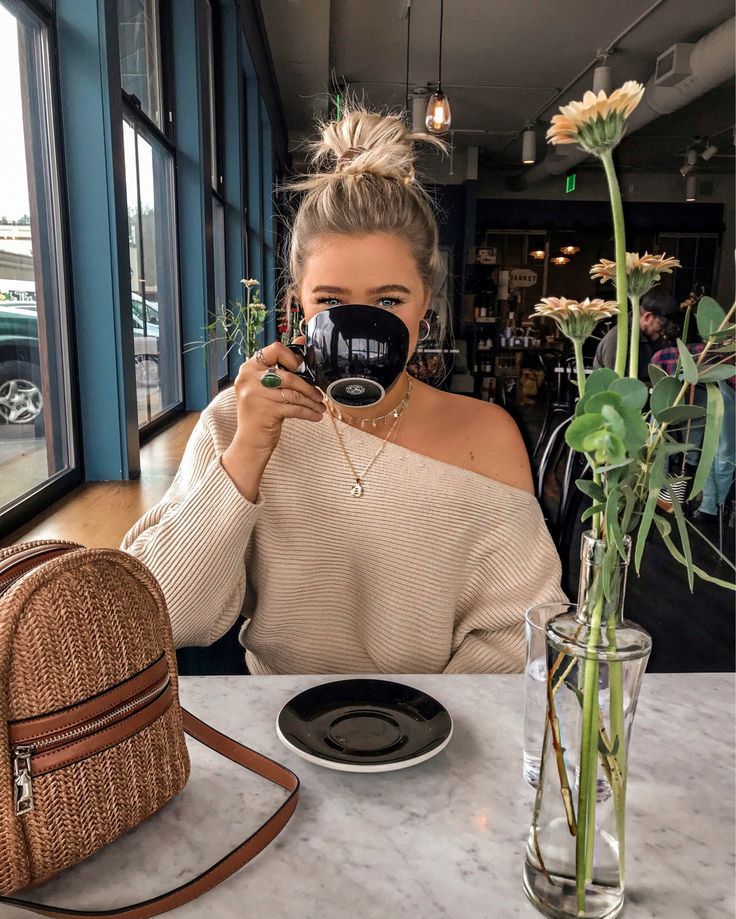 a woman sitting at a table with a coffee cup in front of her and a purse on the other side