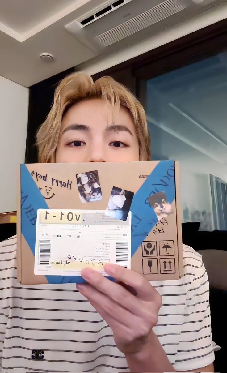 a person holding up a cardboard box with photos on it and an envelope in front of their face