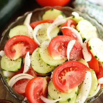 a glass bowl filled with cucumber and tomatoes on top of a wooden table