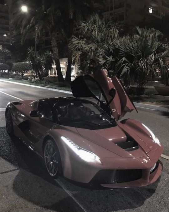 a pink sports car is parked on the side of the road at night with its doors open