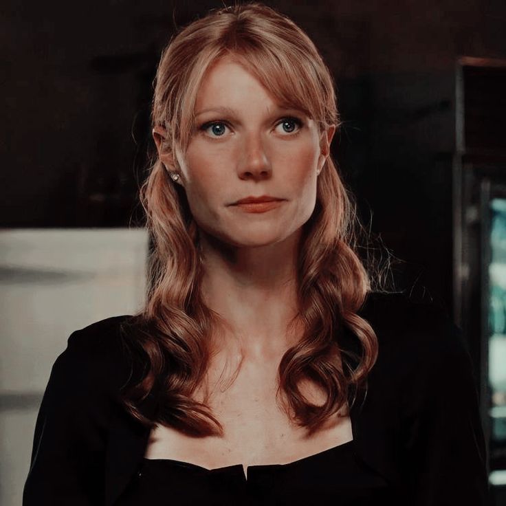 a woman with long hair and blue eyes looks into the camera while standing in a dark room